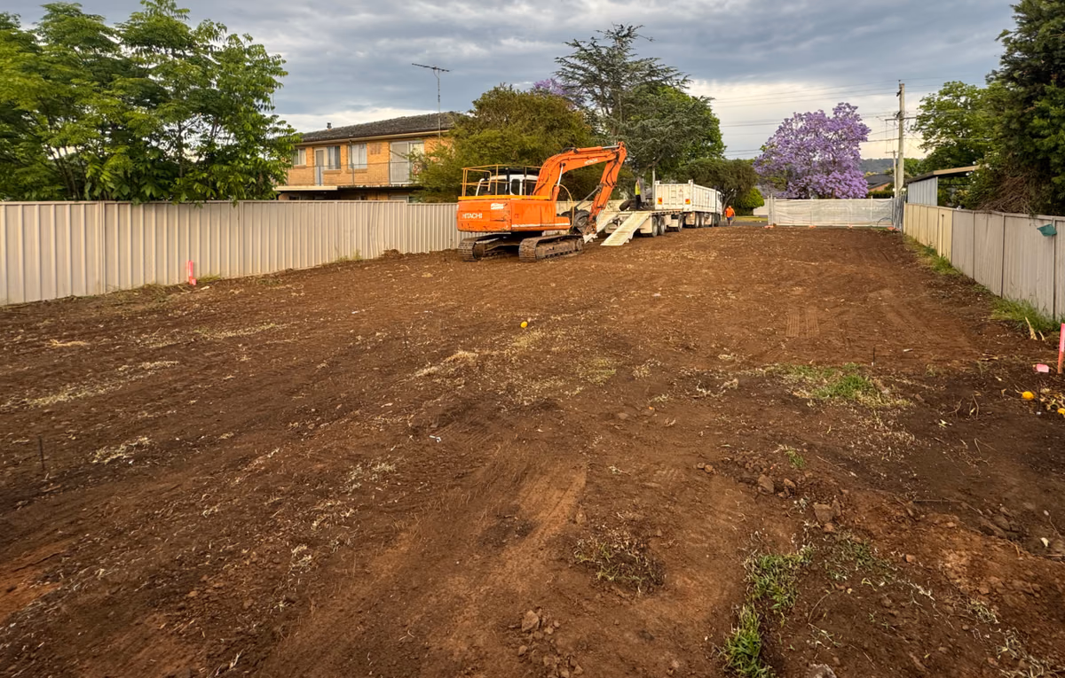 AJ excavator and truck at a cleared residential demolition site