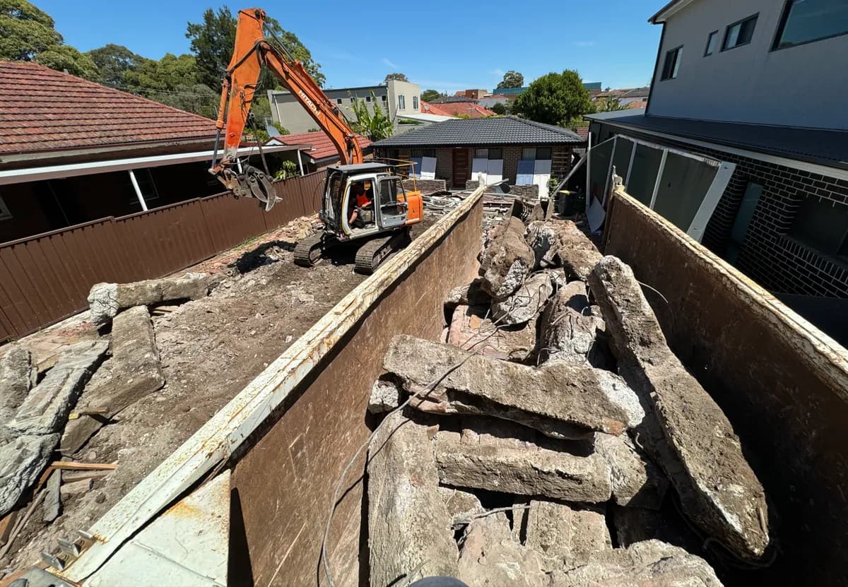 AJ excavator loading concrete footings beside retained residential structures