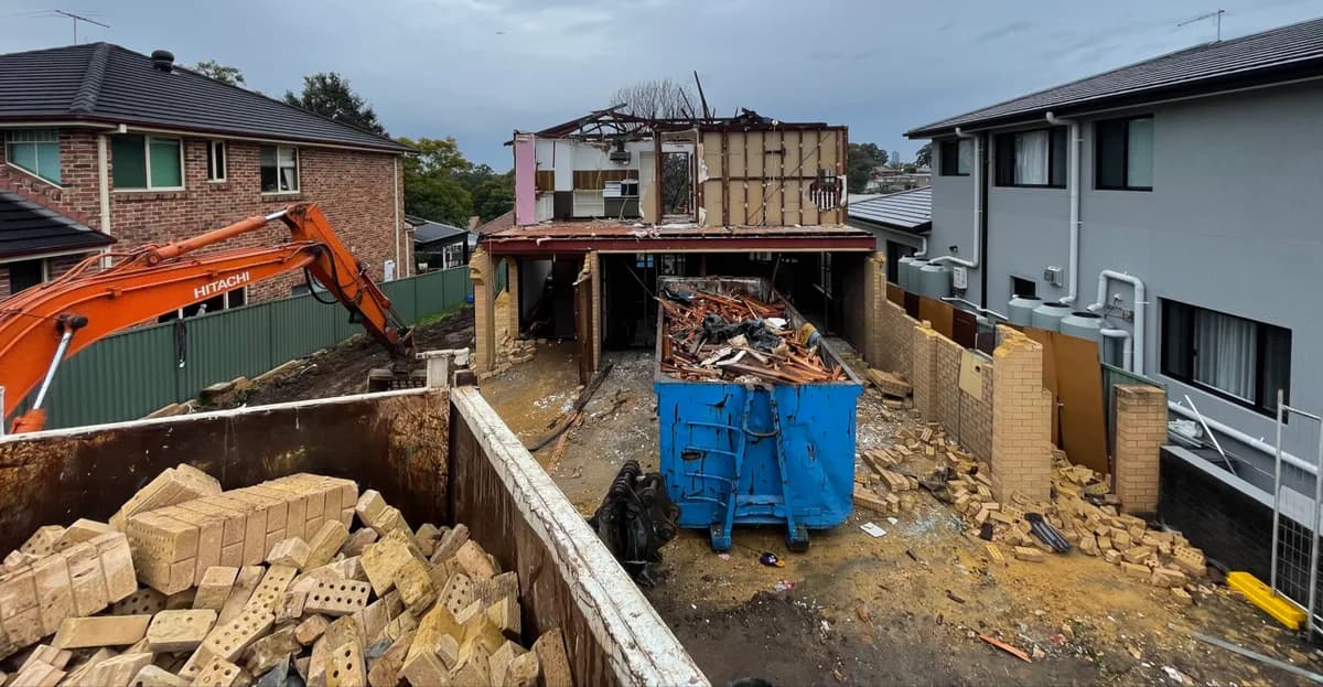 House demolition with an excavator and separate bins containing bricks and other demolition material